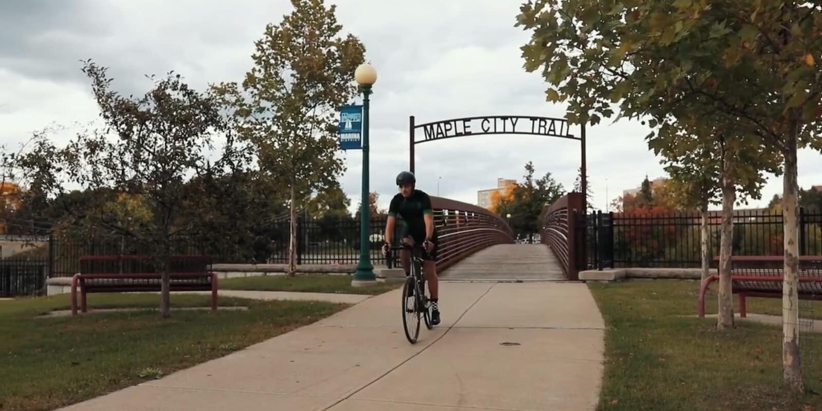 man riding a bike under the maple city trail sign in ogdensburg