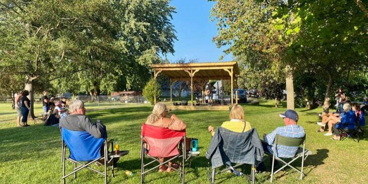 people sitting in chairs at the park watching live music